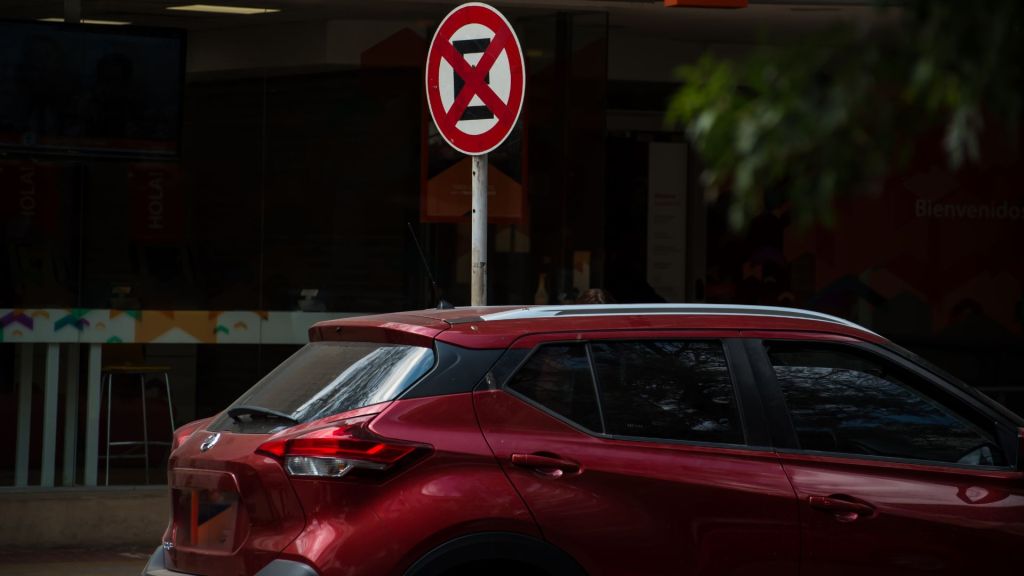Traseira de um carro SUV vermelho parado na rua, bem abaixo de uma placa redonda vermelha de "proibido estacionar e parar". Contexto para quem busca "como saber se levei multa no mesmo dia".