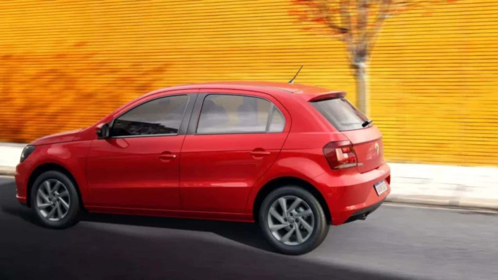 Carro vermelho do modelo Gol, na estrada com fundo laranja.