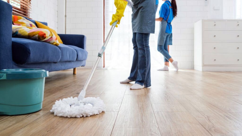 mulher com luvas de limpeza passando um mop no chão da sala