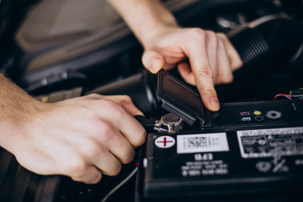 Mãos apontando e mexendo em uma bateria de carro
