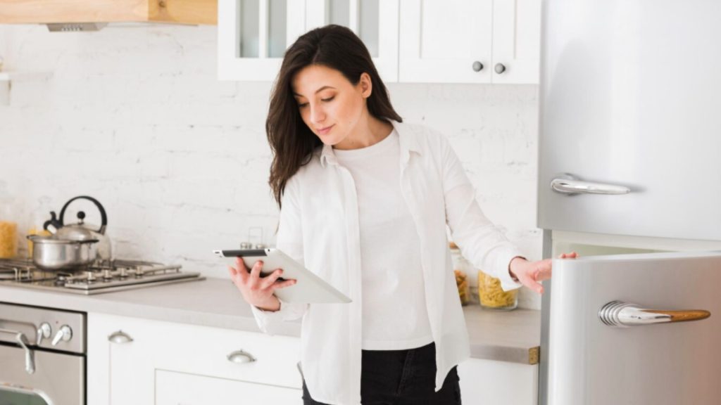 mulher consultando o manual para entender como regular a temperatura da geladeira, enquanto abre a porta do eletrodoméstico