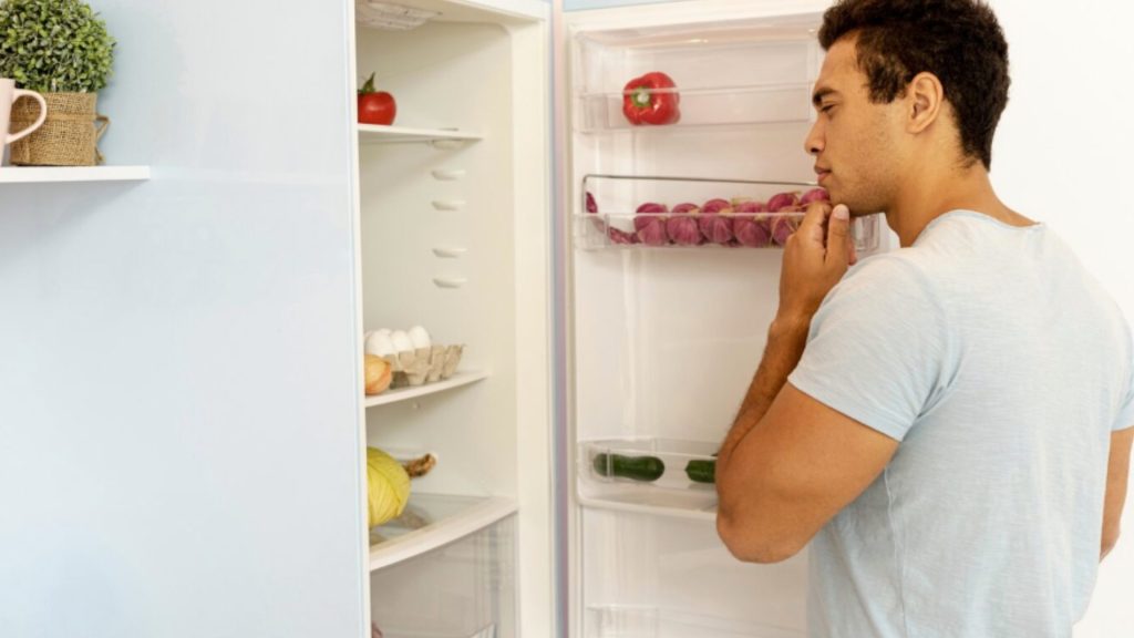 homem olhando para o interior da geladeira com expressão curiosa