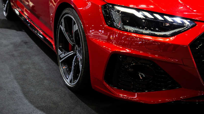 Detalhe do para-lama e farol LED de um Audi RS5 vermelho, realçando a roda esportiva e o design agressivo que contrasta com a proposta de um Audi mais barato