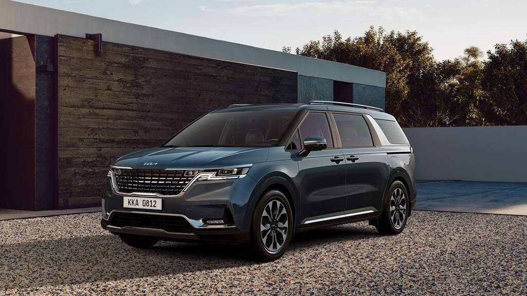 Minivan Kia Carnival azul estacionada em uma área residencial moderna.