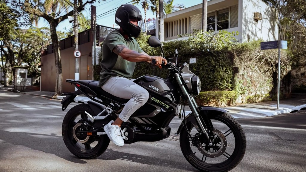 Homem pilotando um das melhores motos elétricas, Watts W125 preta em rua residencial.
