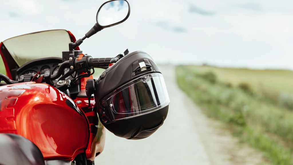 Melhor moto elétrica: capacete preto pendurado em moto vermelha com estrada ao fundo.