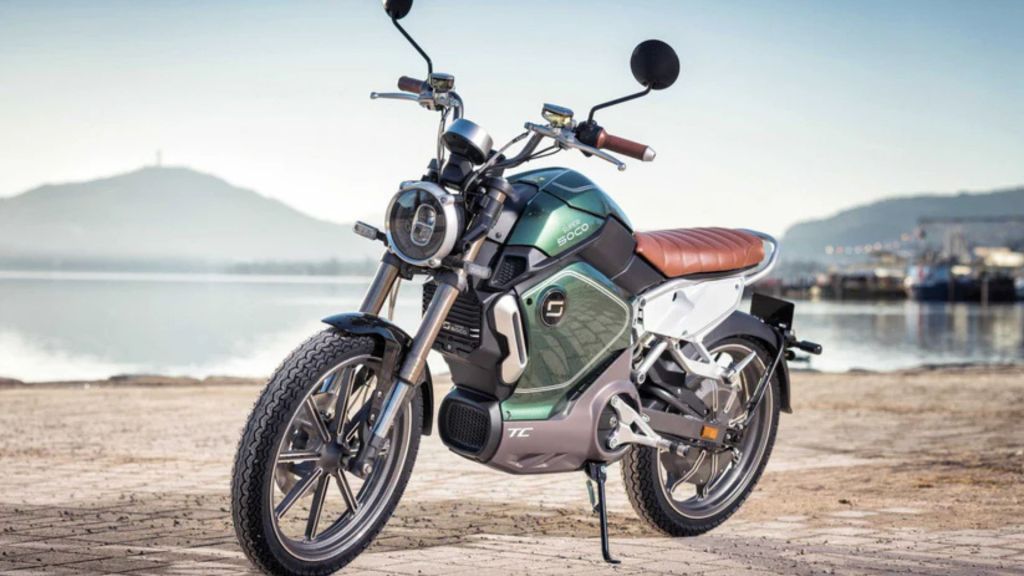 Moto elétrica Super Soco TC verde e marrom estacionada na praia.