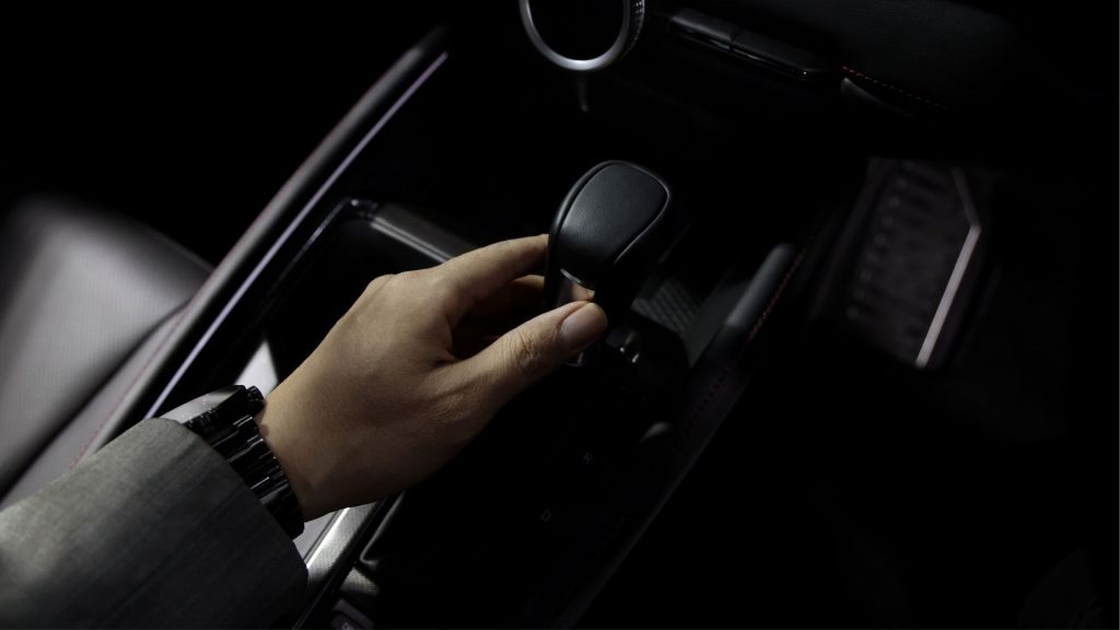 Visão aproximada de uma mão trocando marchas em uma manopla manual, comparada ao conforto do câmbio automático.