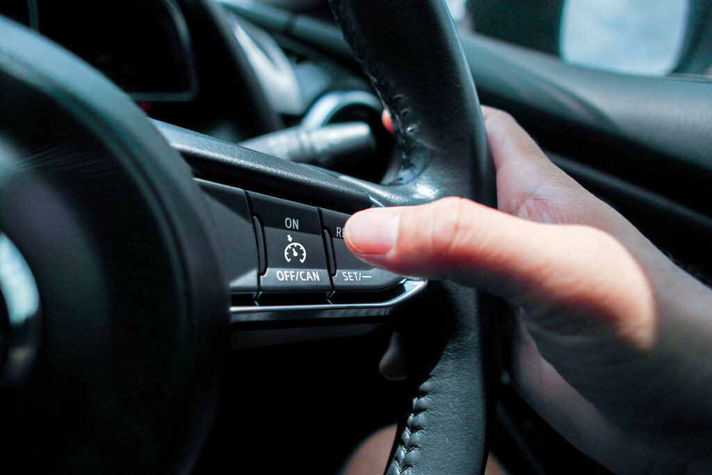 Mão de uma pessoa pressionando um botão de controle no volante de um carro