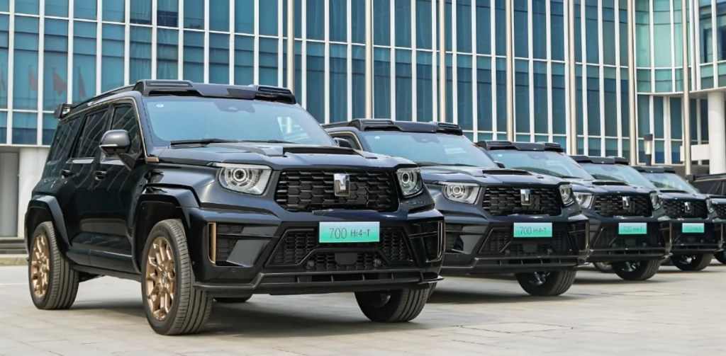 Diversos carros GWM Tank 700 pretos estacionados enfileirados à frente de um prédio.