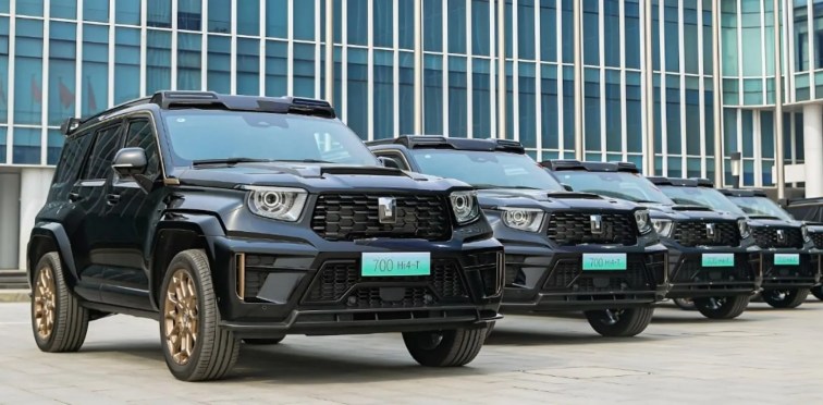 Diversos carros GWM Tank 700 pretos estacionados enfileirados à frente de um prédio.