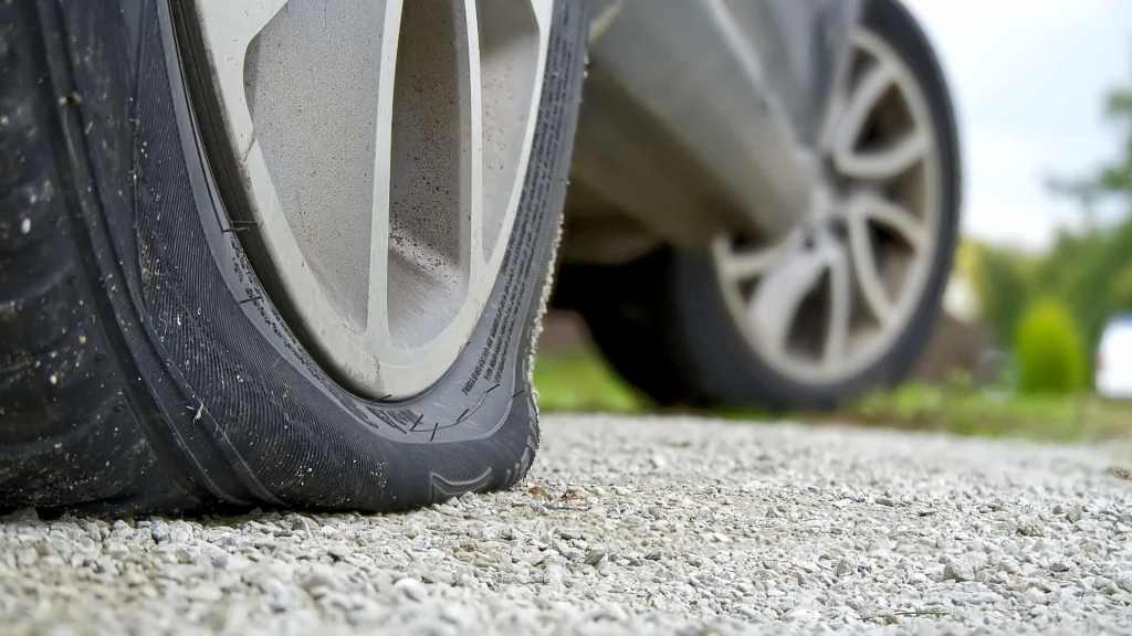 Pneu murcho de carro apoiado no chão de cascalho, evidenciando uma situação comum de furo; a tecnologia pneu seal inside ajuda a vedar pequenas perfurações e evitar esse problema.