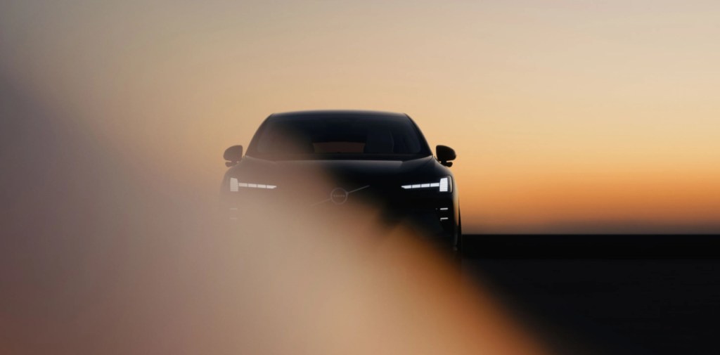Volvo EX60 2026 em imagem teaser mostrando a dianteira iluminada com faróis em LED ao pôr do sol