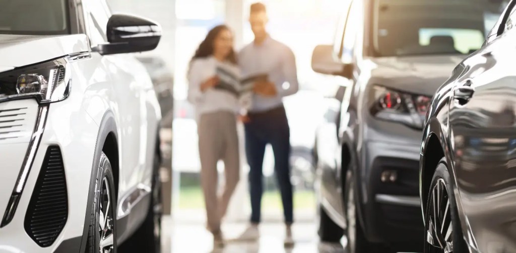 Imagem de casal analisando carros em concessionária, comparando opções e avaliando modelos ideais de carros até 45 mil com foco em custo-benefício e escolha consciente.