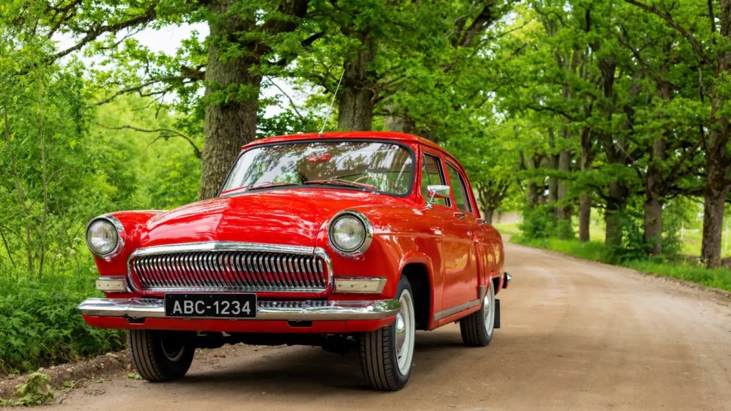 Carro clássico vermelho estacionado em estrada de terra cercada por árvores, com visual bem conservado e placa preta, representando um típico veículo de coleção valorizado no Brasil.