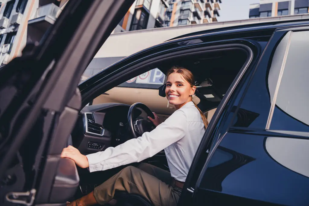 Motorista sorridente entrando em um carro preto moderno em um estacionamento, representando a satisfação e segurança ao escolher um veículo bem avaliado.